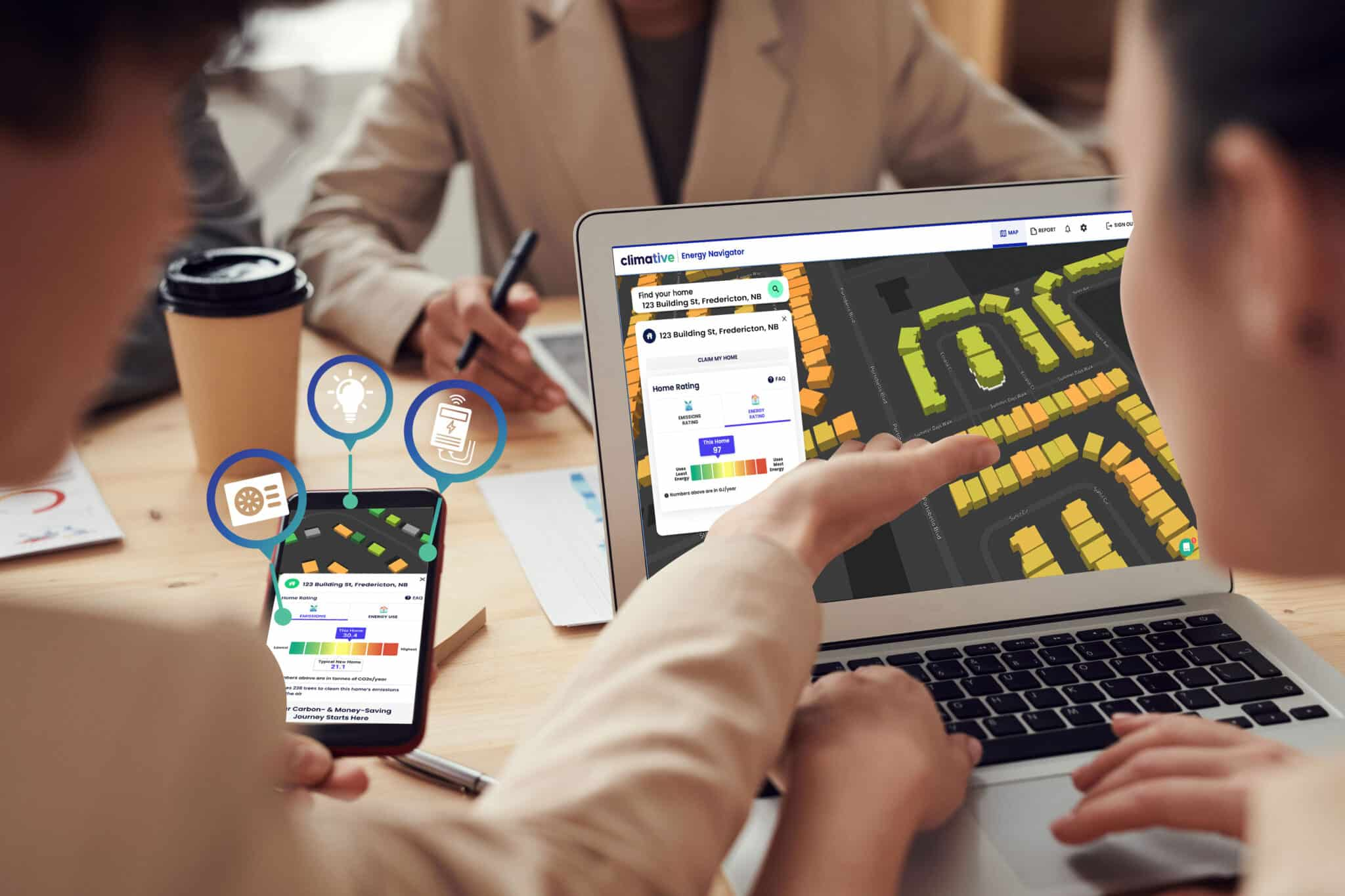 Close-up of two people collaborating on a laptop and smartphone, viewing a software interface showing a map and energy data.