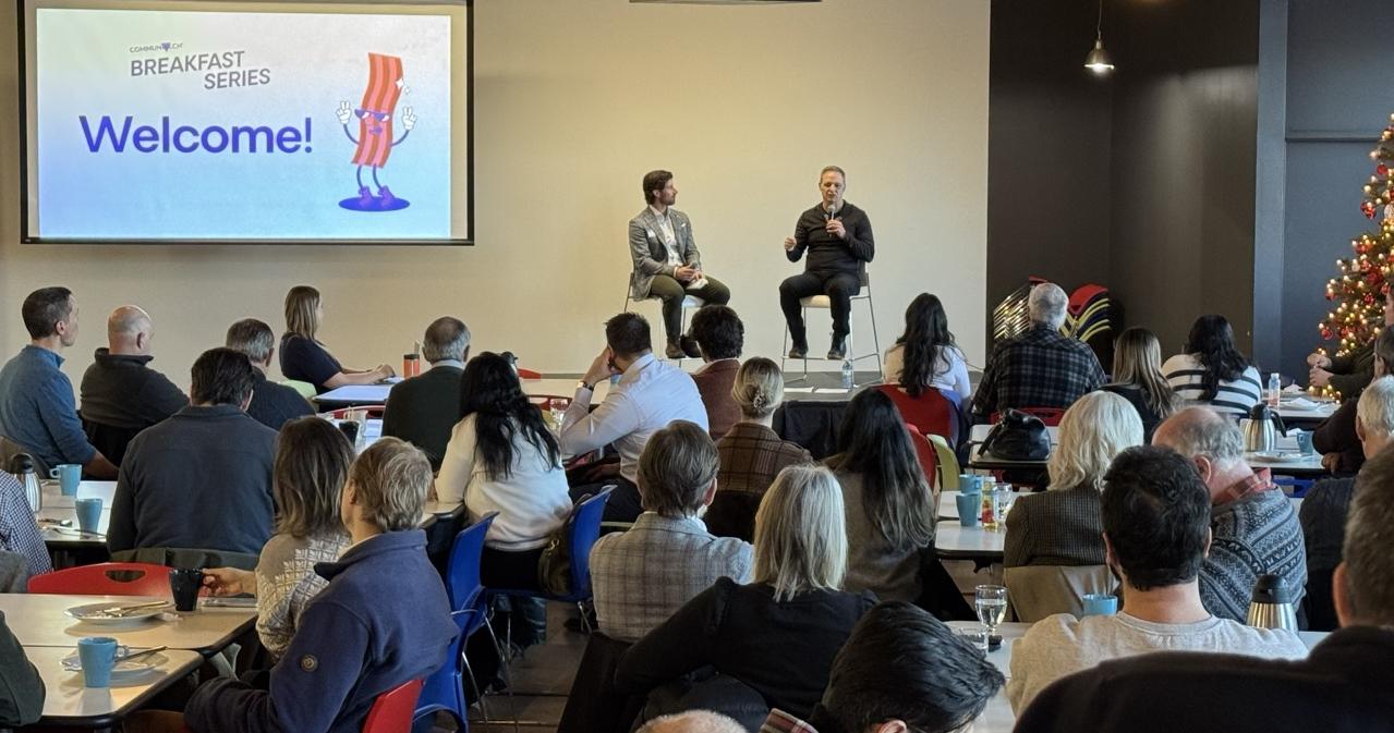 Two men sitting on a stage having a conversation in front of a projector screen that reads 