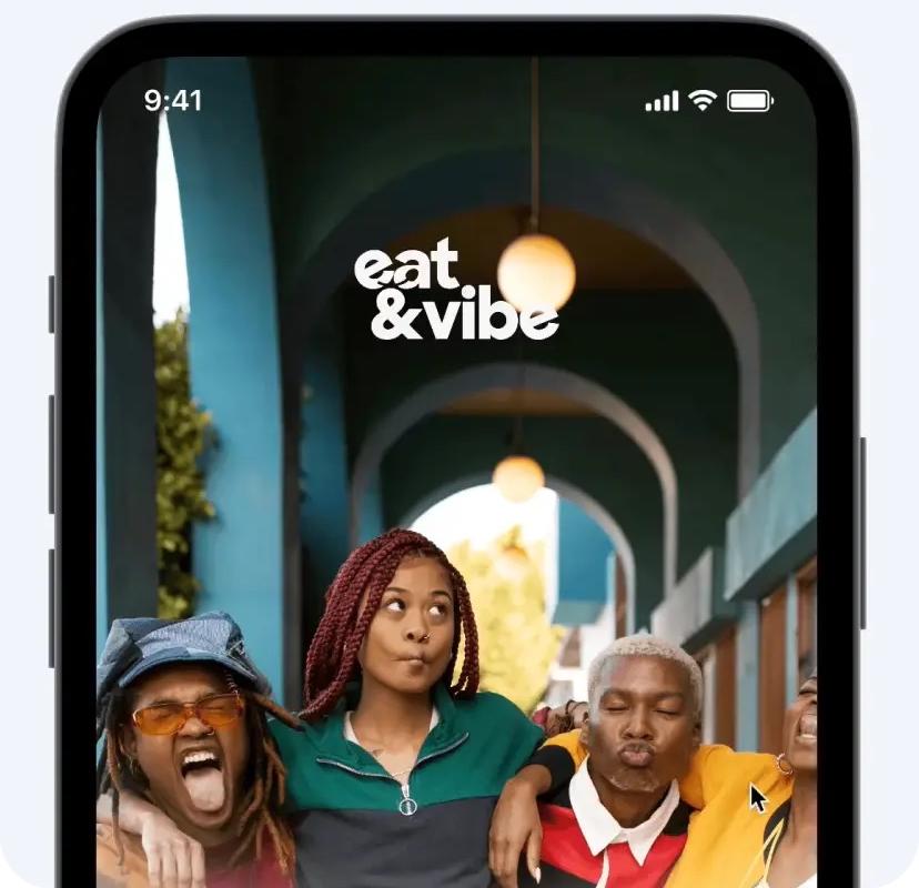Close-up of a smartphone screen showing the 'eat & vibe' app with a vibrant image of three friends posing, illustrating a social or lifestyle-focused application interface.