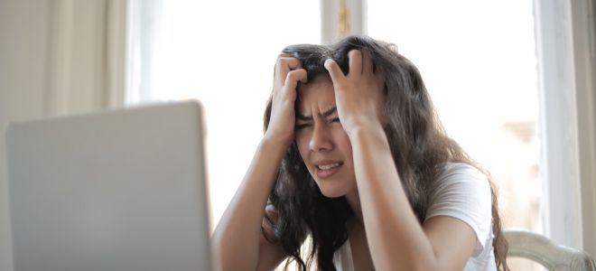 A woman holds head in hands in frustration while looking at computer.