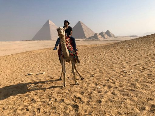 Sam Pasupalak on camel in Egyptian desert, pyramids in the background