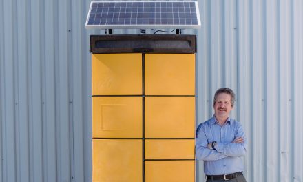 Jim Estill standing beside a yellow storage device with multiple slots and a solar panel at the top known as a "Hive"